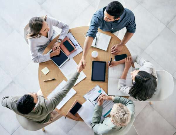Five people sitting around a round table, engaged in discussion with notebooks, tablets, and smartphones during their business English classes.