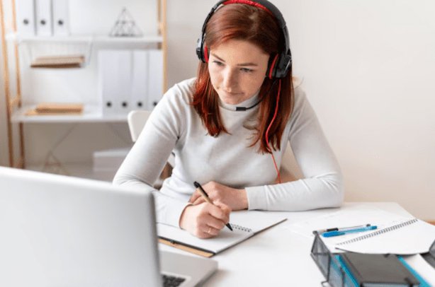 In a bright room, a girl with headphones is jotting down notes while engaging with their English learning WhatsApp group.