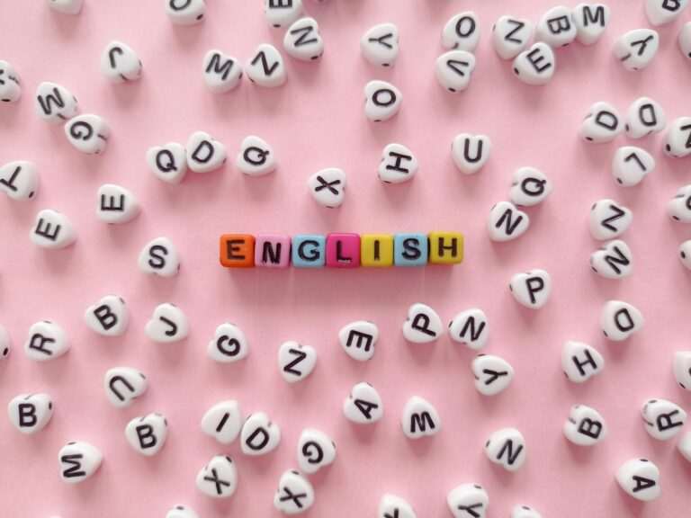 Colorful letter beads spell "ENGLISH" on a pink background, symbolizing the vibrant journey of learning English online, surrounded by scattered white beads with black letters.