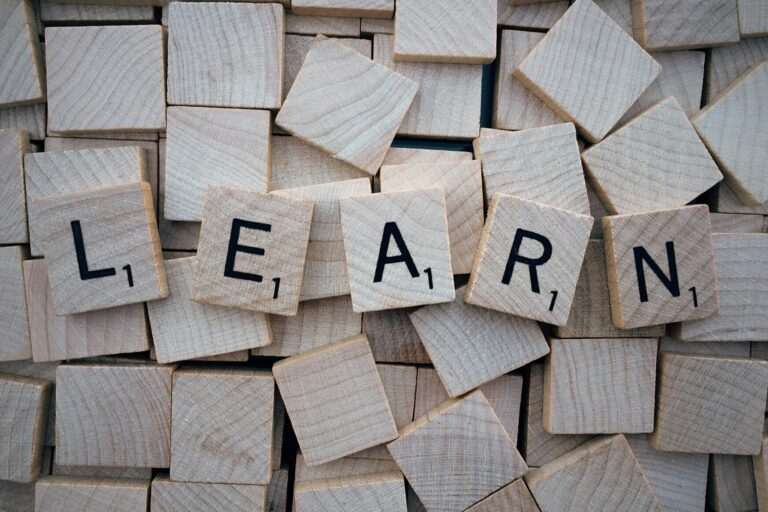 Wooden letter tiles spell out the word "LEARN" on a scattered background of blank tiles, capturing the spirit of an English learning WhatsApp group.