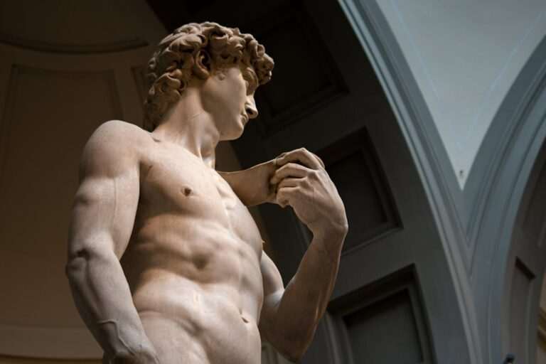 An English-speaking online forum discusses the majestic marble statue of a muscular male figure, seen from below with a sling over his shoulder, set against an arched architectural background.