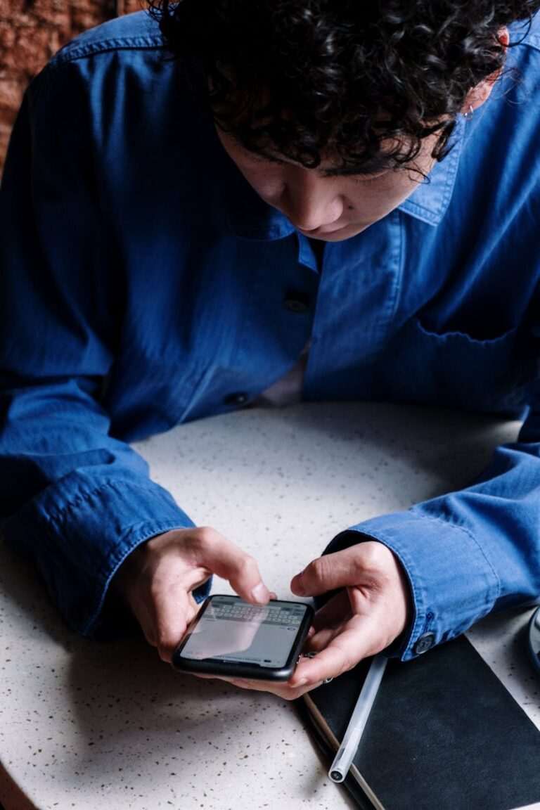A person in a blue shirt is using a smartphone, possibly joining an English learning WhatsApp group link, while sitting at a table with a notebook and pen.